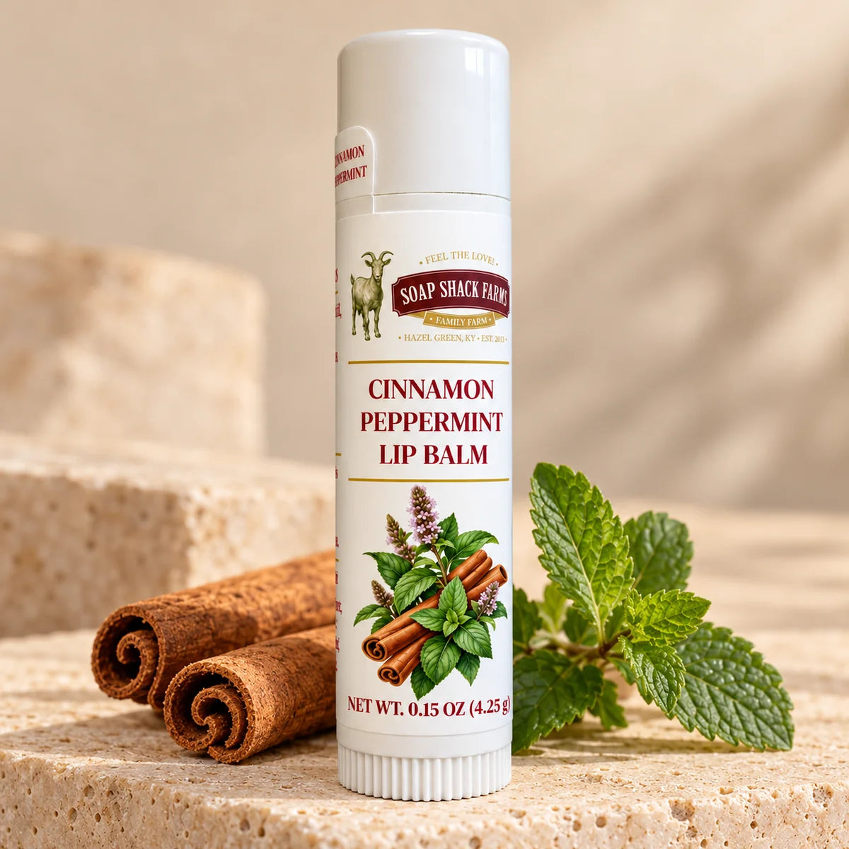 Soap Shack Farms Cinnamon Peppermint lip balm displayed on pale stone with cinnamon sticks and fresh peppermint leaves.