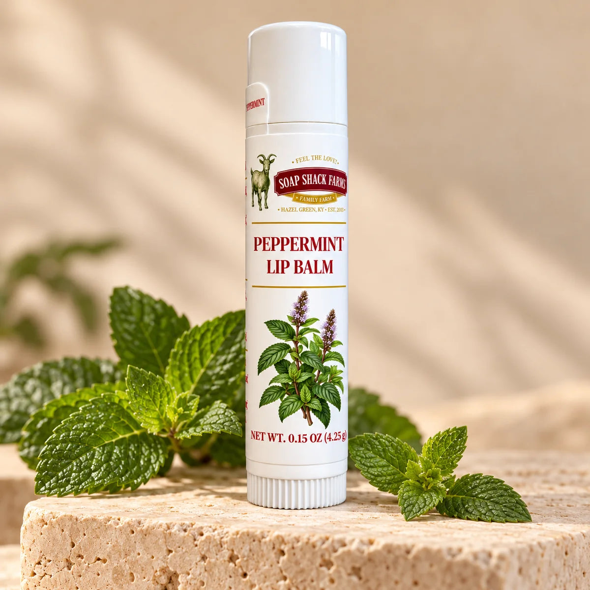 Soap Shack Farms Peppermint Lip Balm in a white 0.15 oz tube on a stone surface with flavor-inspired botanicals in a warm studio setting.