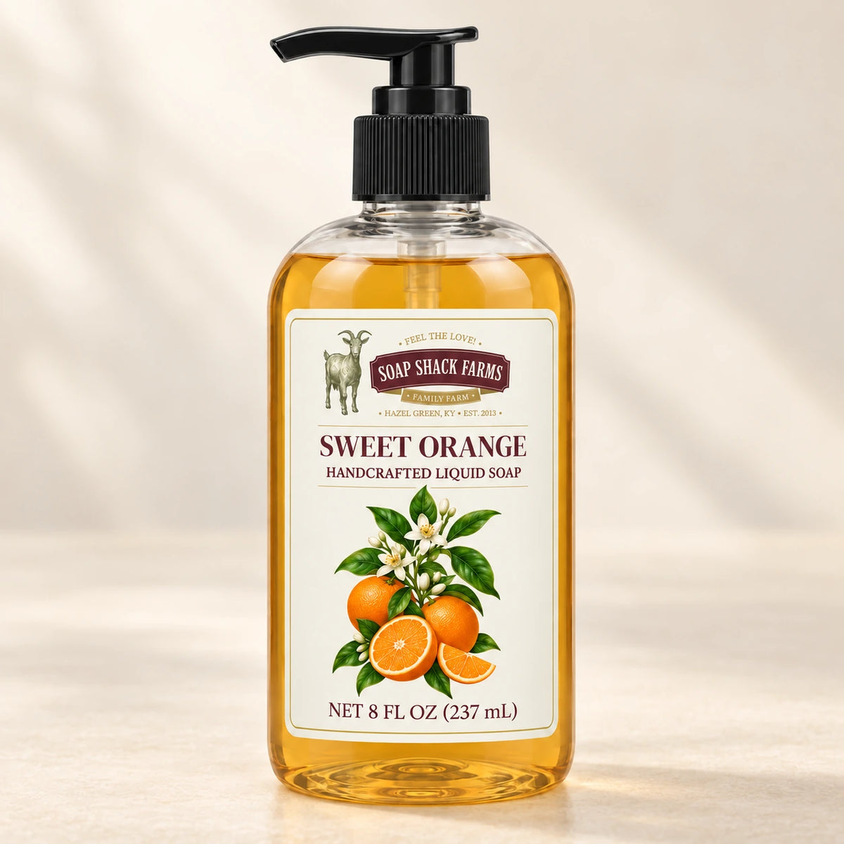 Sweet Orange handcrafted liquid soap in a clear pump bottle on a warm cream studio background.