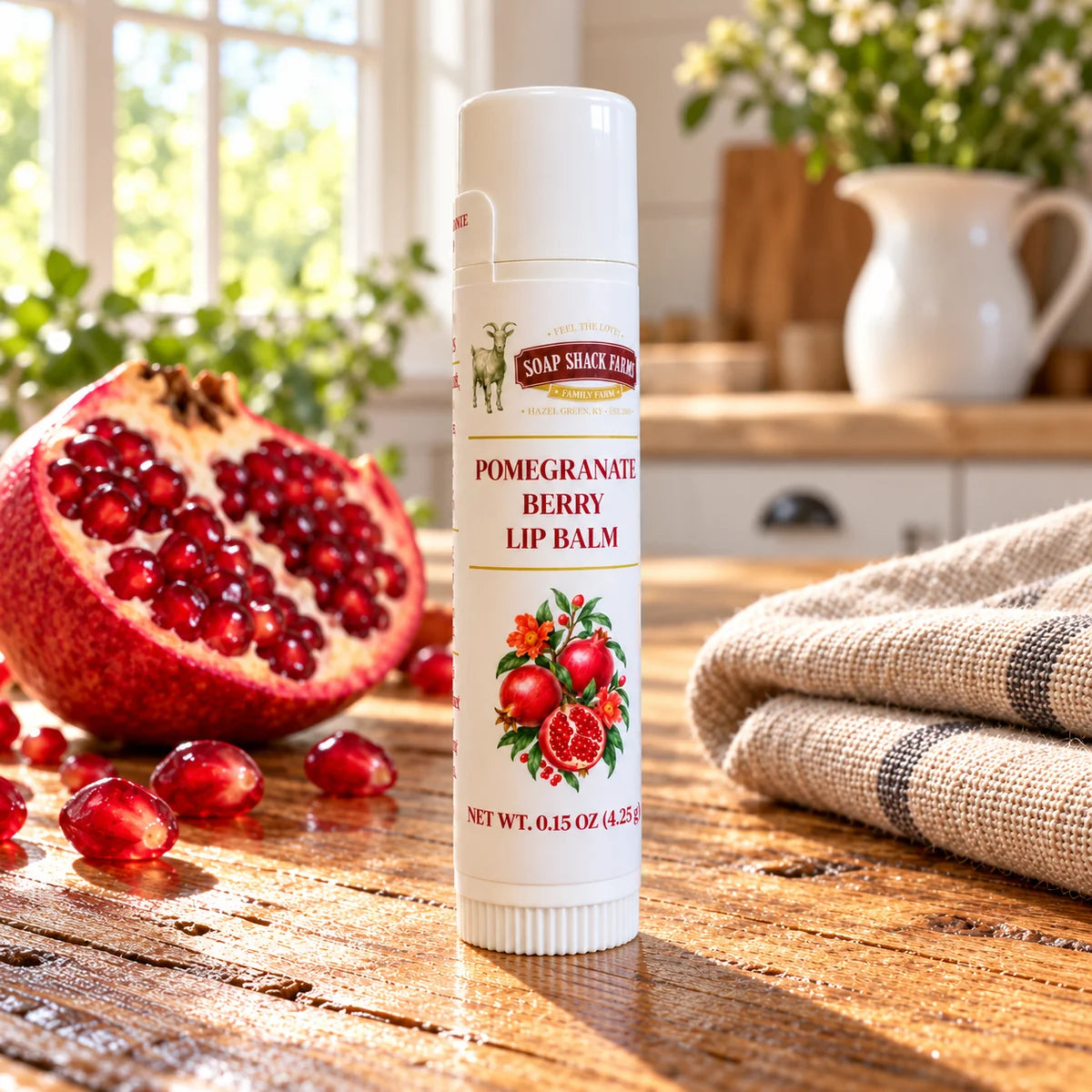 Soap Shack Farms Pomegranate Berry lip balm on a stone pedestal beside a cut pomegranate, seeds, and green leaves.
