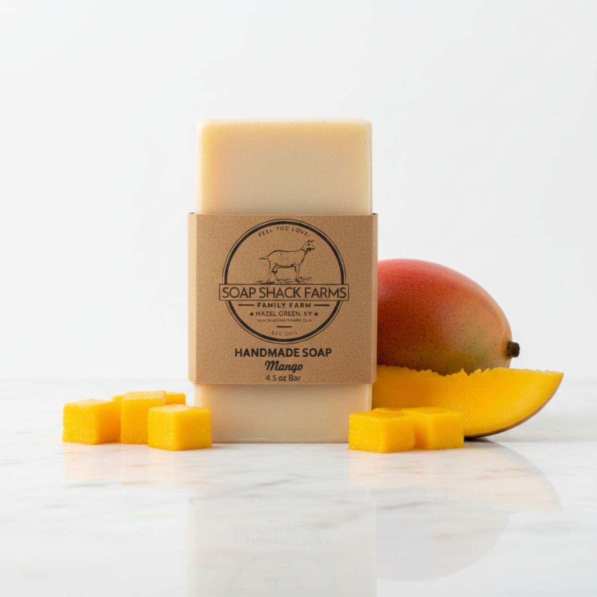 Soap Shack Farms Mango Handmade Soap 4.5 oz bar with kraft paper label, fresh mango and mango cubes on marble surface