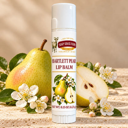 Soap Shack Farms Bartlett Pear Lip Balm in a white 0.15 oz tube on a stone surface with flavor-inspired botanicals in a warm studio setting.