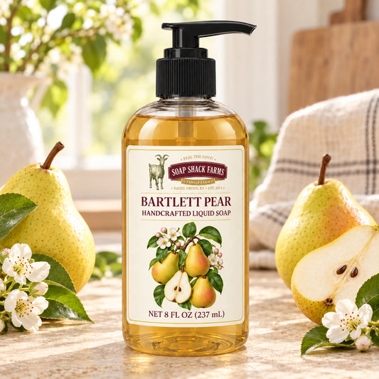 Bartlett Pear handcrafted liquid soap with ripe pears, a sliced pear, white blossoms, and farmhouse linen in a sunlit setting.
