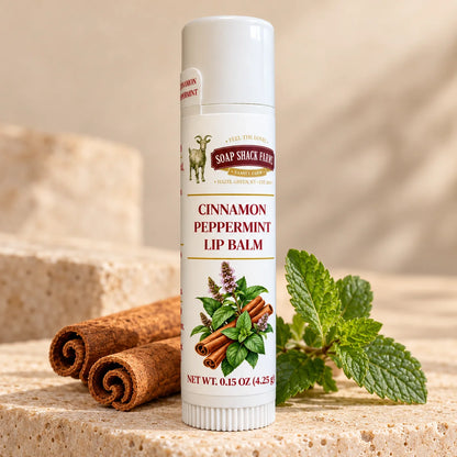 Soap Shack Farms Cinnamon Peppermint lip balm displayed on pale stone with cinnamon sticks and fresh peppermint leaves.