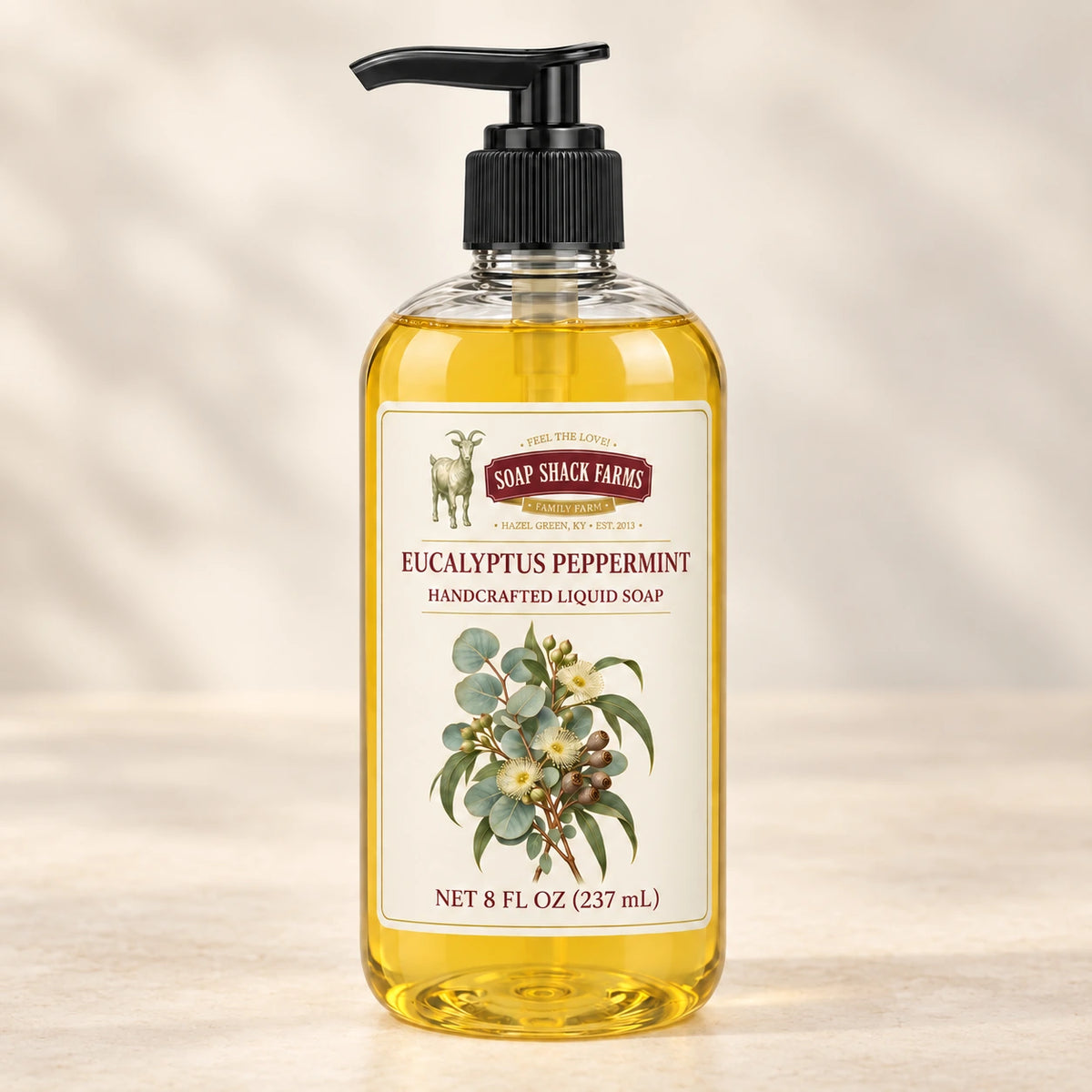 Eucalyptus Peppermint handcrafted liquid soap in a clear pump bottle on a warm cream studio background.