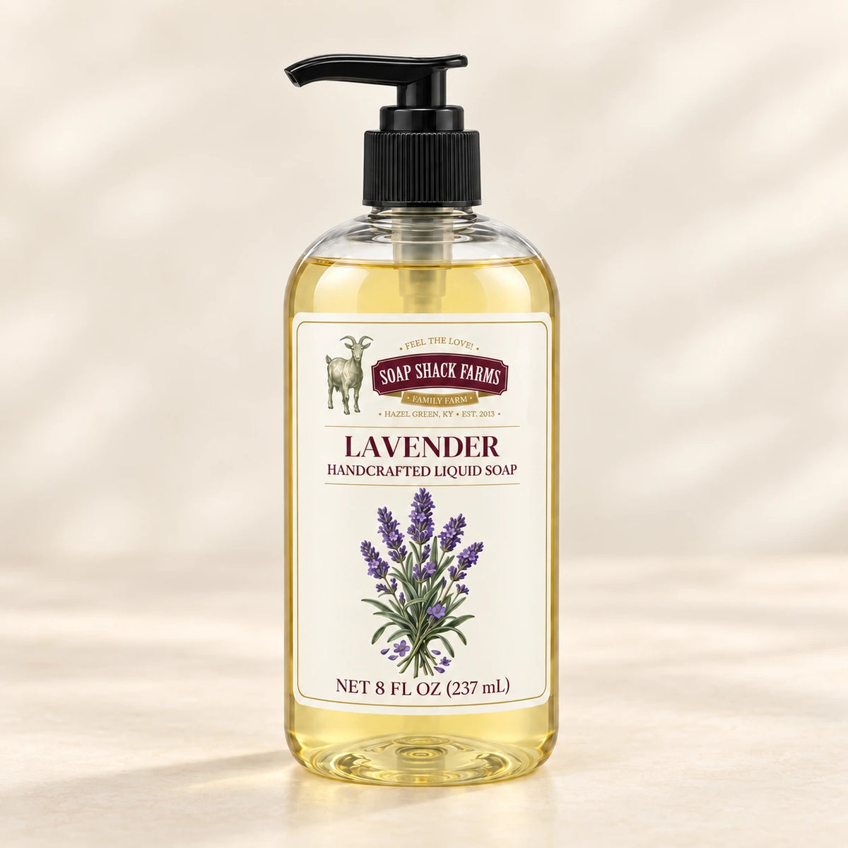 Lavender handcrafted liquid soap in a clear pump bottle on a warm cream studio background.