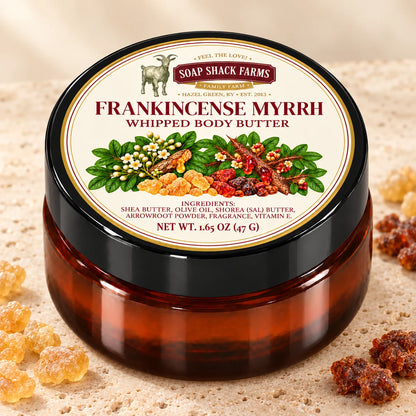 Frankincense Myrrh Whipped Body Butter in an amber jar on pale stone with golden and reddish resin accents.