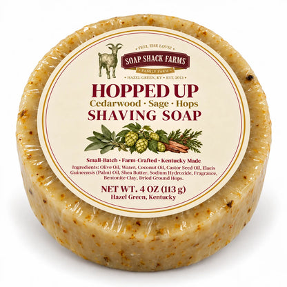 Round speckled Hopped Up shaving soap by Soap Shack Farms, wrapped with a cream botanical label on a white background.