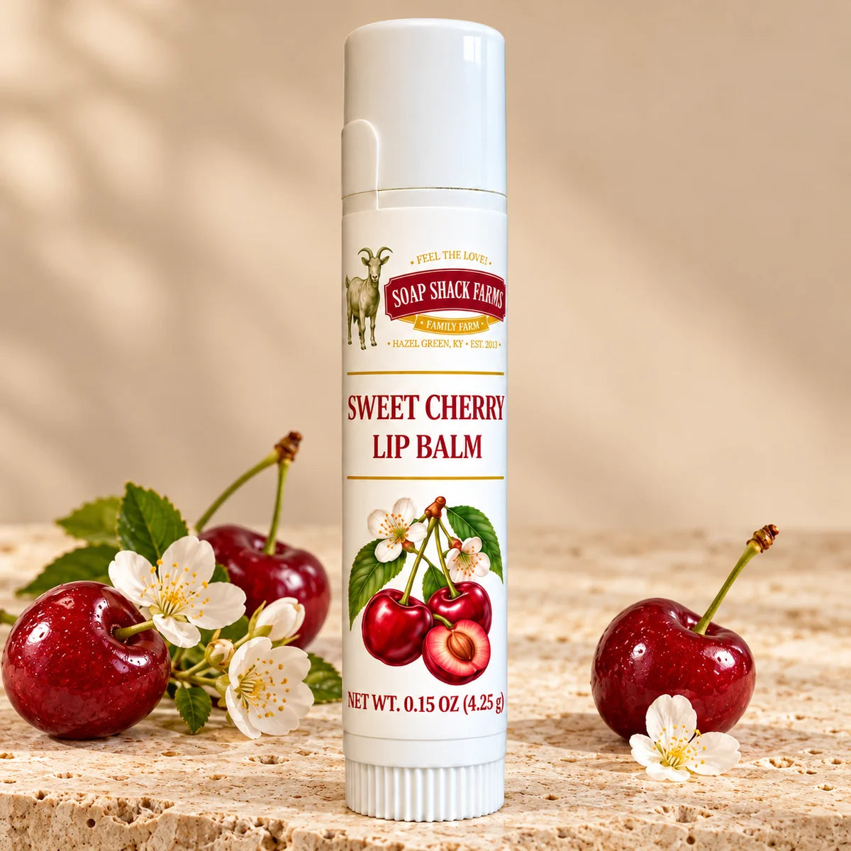 Soap Shack Farms Sweet Cherry Lip Balm in a white 0.15 oz tube on a stone surface with flavor-inspired botanicals in a warm studio setting.