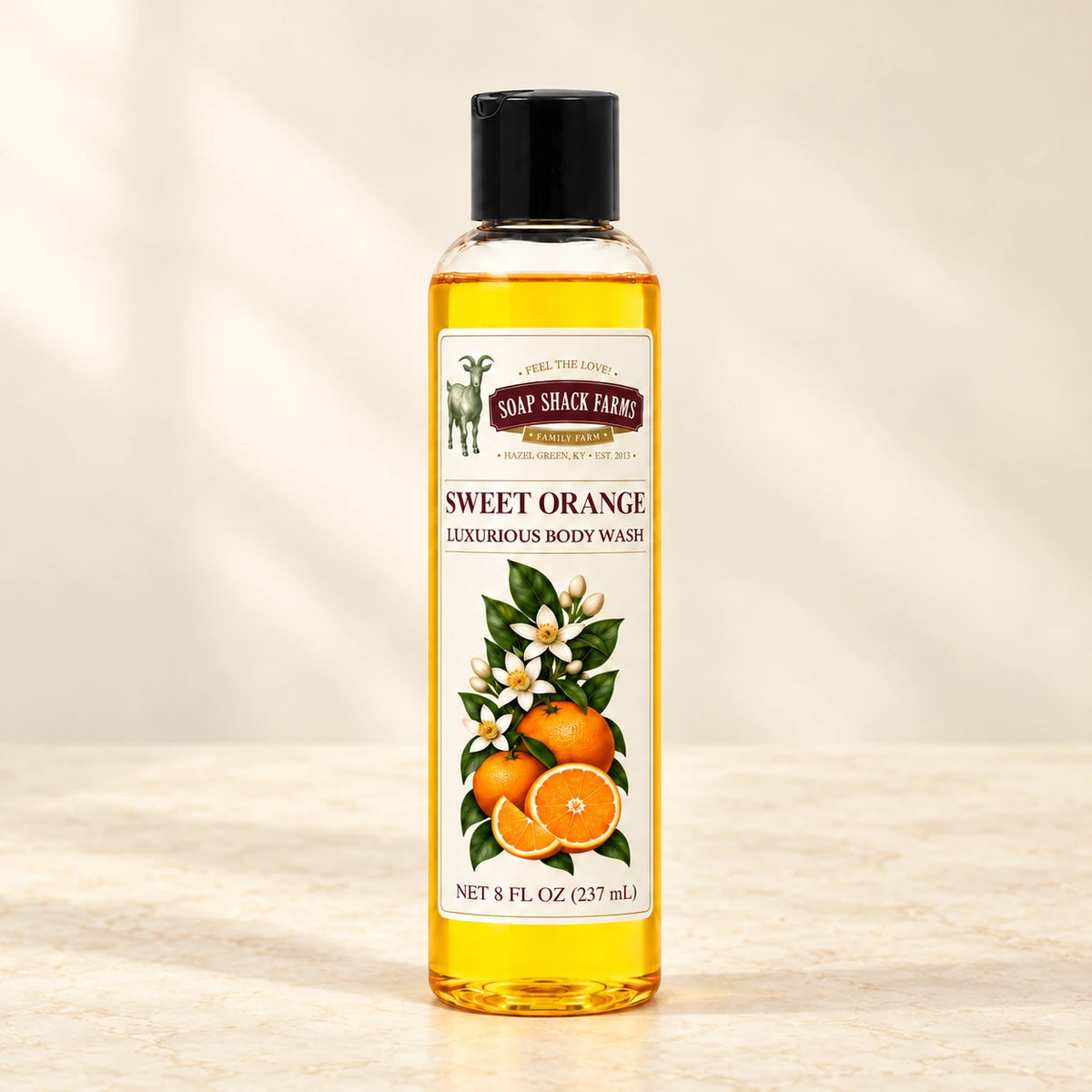 Sweet Orange luxurious body wash in a slender clear bottle on a warm cream studio background.