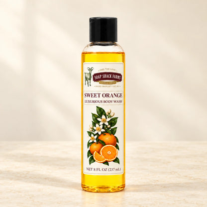 Sweet Orange luxurious body wash in a slender clear bottle on a warm cream studio background.