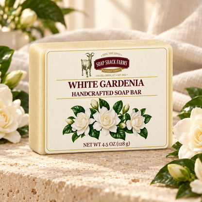 White Gardenia olive oil soap bar on warm cream stone with white gardenia blooms and glossy leaves.